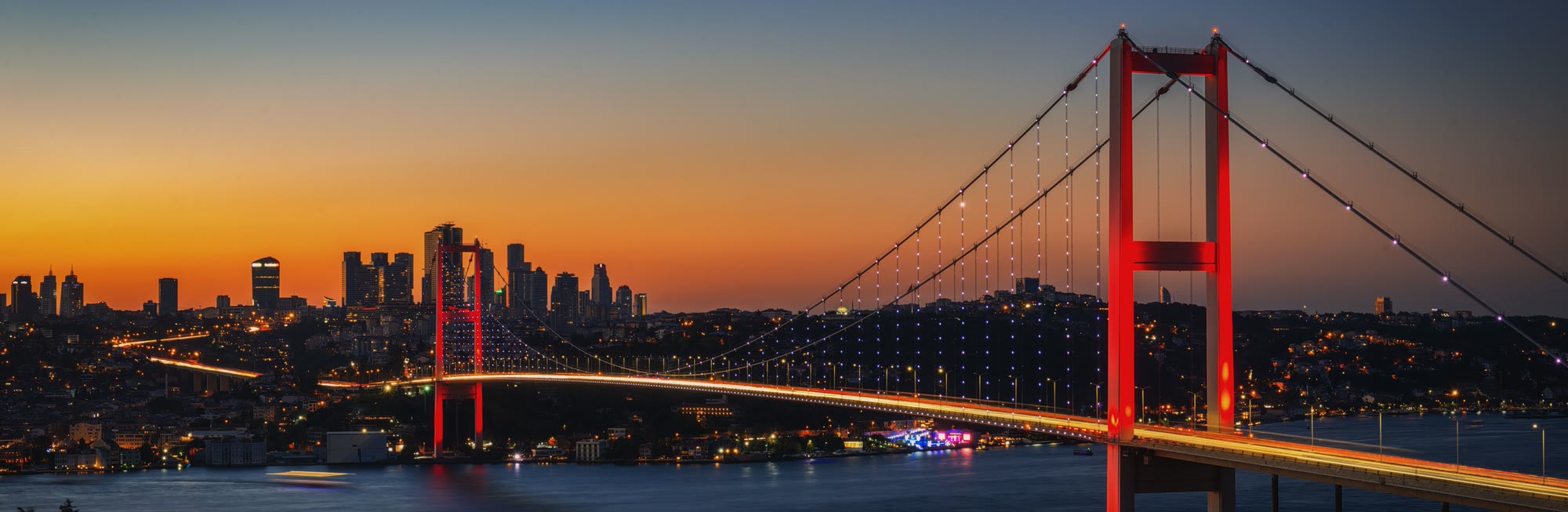 Bosphorus Bridge lit red at dusk with the Istanbul skyline