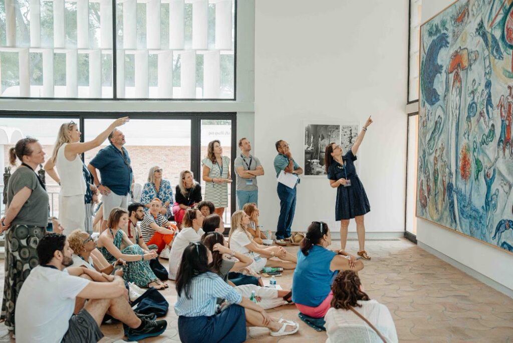 IRG programme participants gathered in a gallery, looking up at a large painting as the guide points to it.