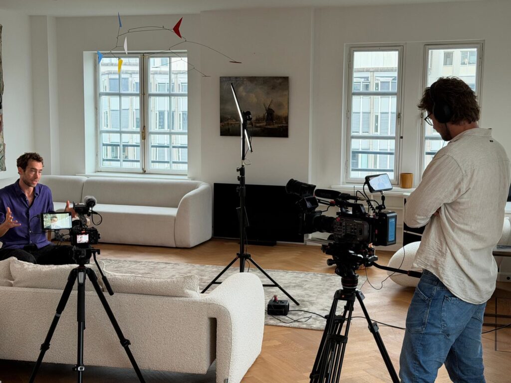 A video shoot in the IRG office: one person speaks to camera on a sofa while a camera operator in headphones watches.